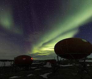 Two googie huts in foreground, one with light shining through window, with green aurora above