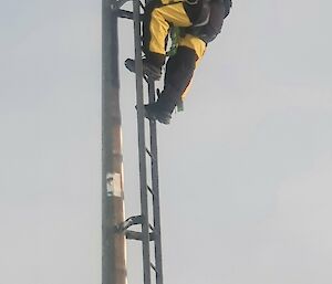 A man in bright yellow safety equipment at the top of a mast