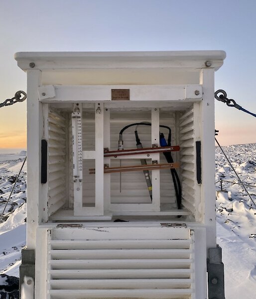 A white box with luvres with  a weather instrument inside