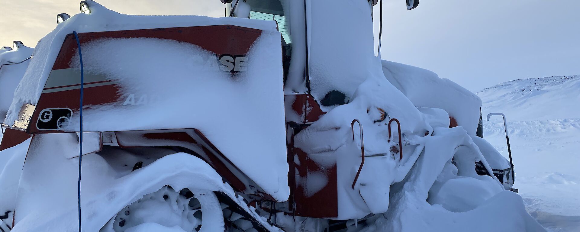 A red Quadtrac tractor. Its wheels and tracks and most of its body are caked in thick clumps and layers of snow.