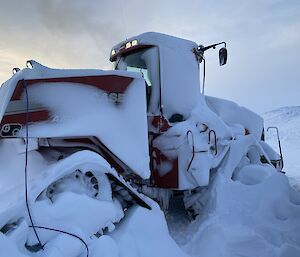 A red Quadtrac tractor. Its wheels and tracks and most of its body are caked in thick clumps and layers of snow.