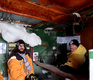 Three people stand in cold porch of old building which has peeling point on walls, and snow inside