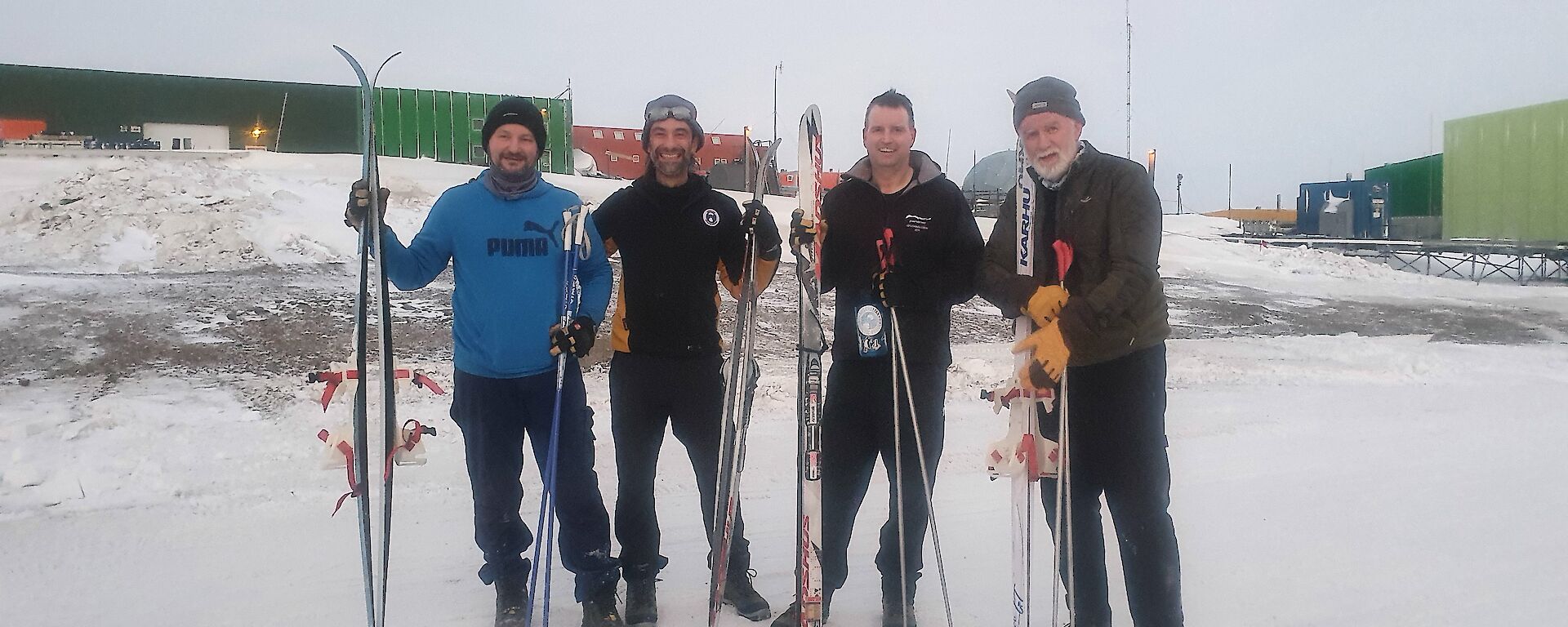 Four men standing in the snow with skis and poles