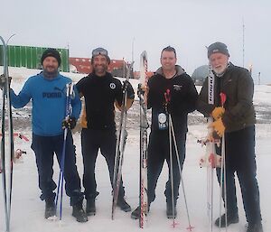 Four men standing in the snow with skis and poles