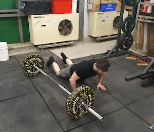 A man on the floor completing a burpee with a barbell next to him