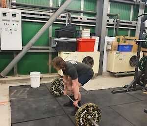 A man in black shorts poised to do a deadlift with a barbell