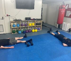 Two men lying on blue mats looking tired
