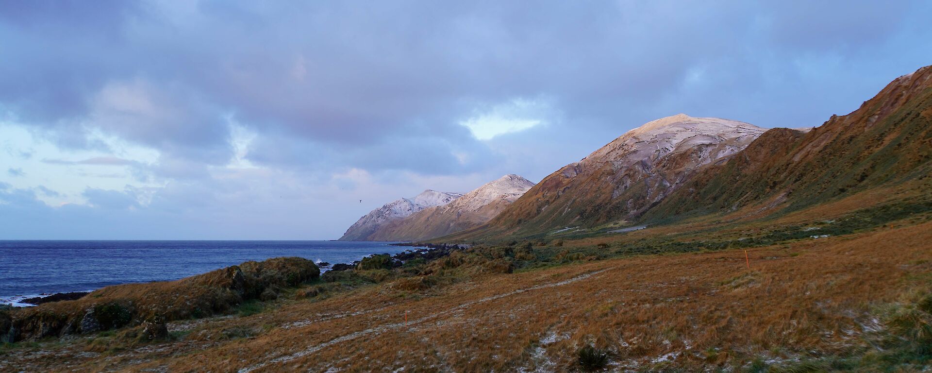 Snow capped hills drop away to the sea under grey clouds