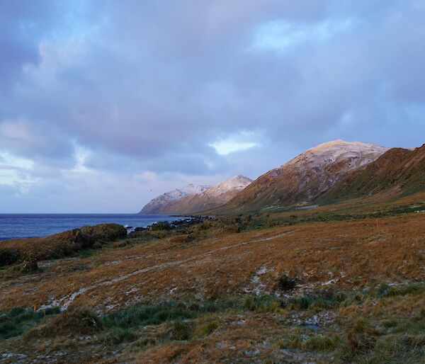 Snow capped hills drop away to the sea under grey clouds