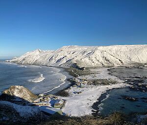 A small island is covered in snow with a bright blue sky surrounding it