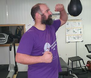 Man in gym dressed in a purple tee shirt hits speed ball with raised left fist