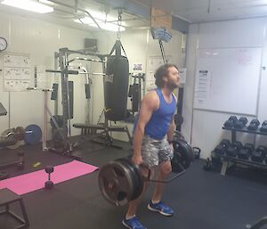 Man in weight gym lifts heavy bar with weights either end