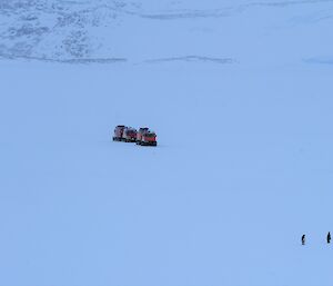 Expanse of white with hagglunds and two emperor penguins seen from a distance