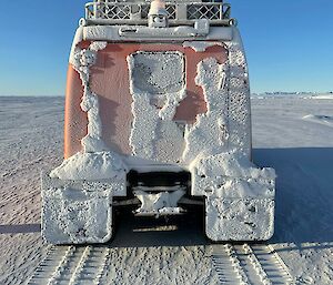 Rear of orange Hagglunds parked on sea ice and covered in snow