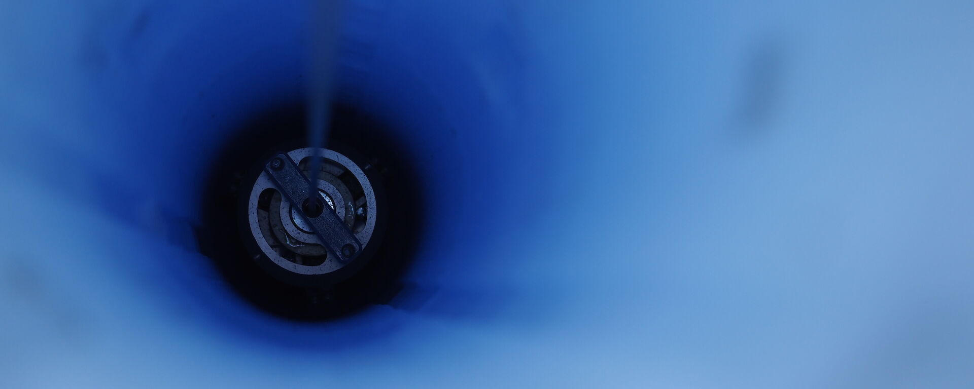 looking down a hole through blue ice with drill inside