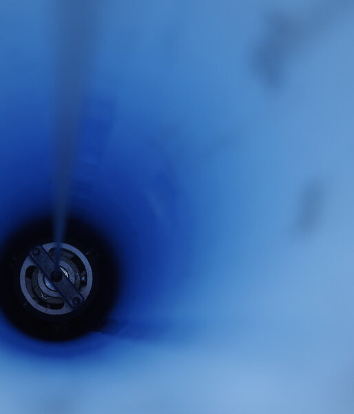 looking down a hole through blue ice with drill inside