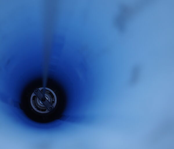 looking down a hole through blue ice with drill inside