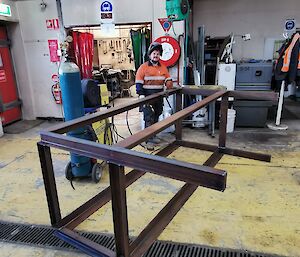 A man in hi-vis standing behind a steel structure with some welding equipment in a workshop