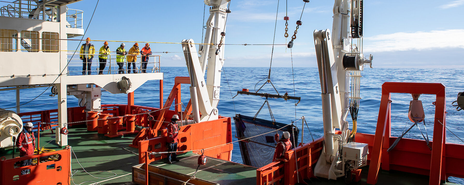 A piece of equipment is lowered into the water from the back of a ship by a large winch