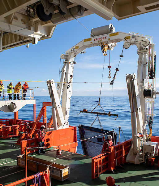 A piece of equipment is lowered into the water from the back of a ship by a large winch