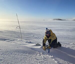 Man in winter gear in a snow covered landscape kneels over a mound in sea-ice checking instruments