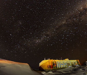 A yellow, rectangular building, beneath a thickly-starred night sky with the glow of the Milky Way stretched across it