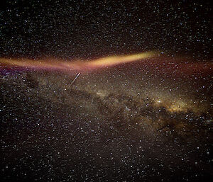 A night sky photo centred on the glow of the Milky Way. Alongside the Milky Way is an optical phenomenon, appearing as streaks of bright yellow-orange and red-purple light