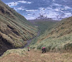 Two people clamber up a steep track from the beach.  Waves breaking on the rocks below.