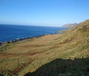 A steep green hill sweeping down towards a blue sea, with a glorious blue sky