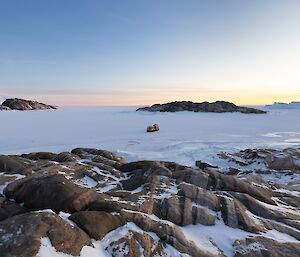 View from top of rocky island, onto sea ice with red hagglunds in the distance