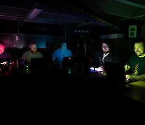 5 people sitting in the dark with laptops