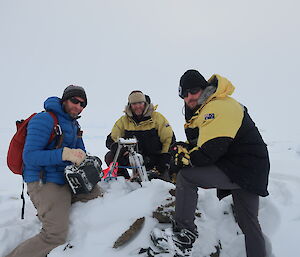 3 men surrounded by snow working on a camera