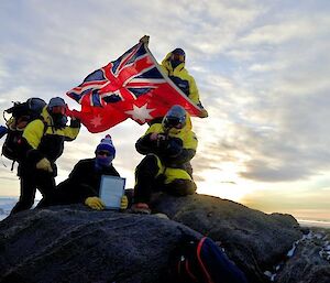 4 men holding up a flag at the top of a hill
