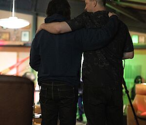 The back view of 2 men with arms around each others shoulders