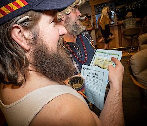 A close-up of a beared man in a singlet looking through some papers