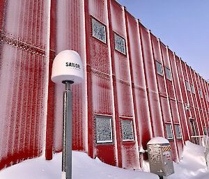 A long, two-storeyed building with a ridged metal exterior painted bright red. Parts of it are dusted lightly with snow, and large piles of snow are banked up against a porch and other places along its front wall