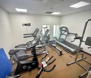 A small room filled with exercise equipment, including two exercise bikes, two treadmills, an elliptical trainer and a rowing machine