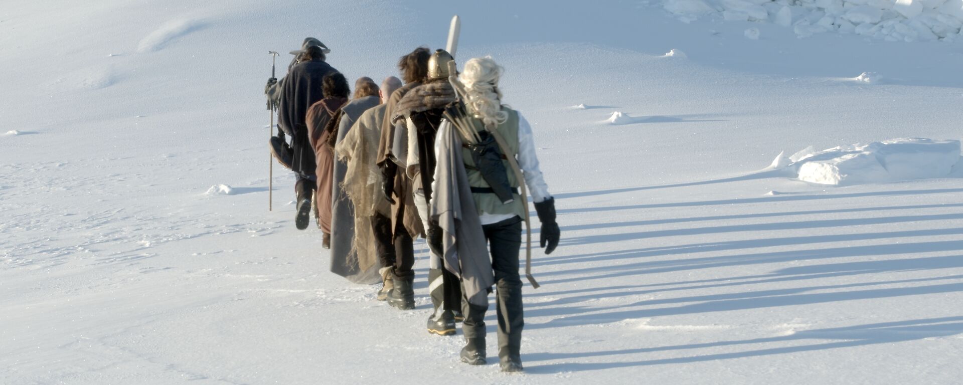 A line of people dressed in Lord of Rings costumes walking away from camera on the snow