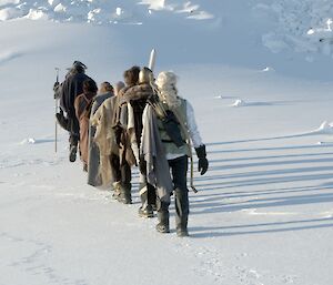 A line of people dressed in Lord of Rings costumes walking away from camera on the snow