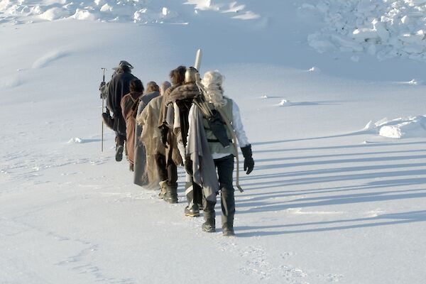 A line of people dressed in Lord of Rings costumes walking away from camera on the snow