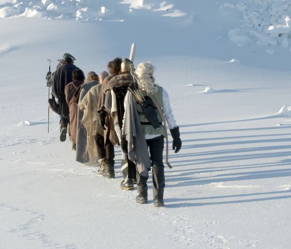 A line of people dressed in Lord of Rings costumes walking away from camera on the snow