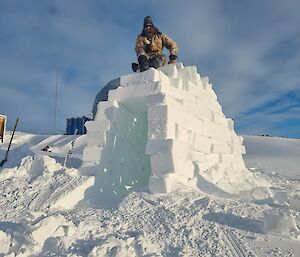 Man sits on top of igloo made from large square ice blocks
