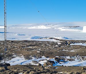 Rocky foreground with large metal mast up right of picture. Man in distance is laying cable.