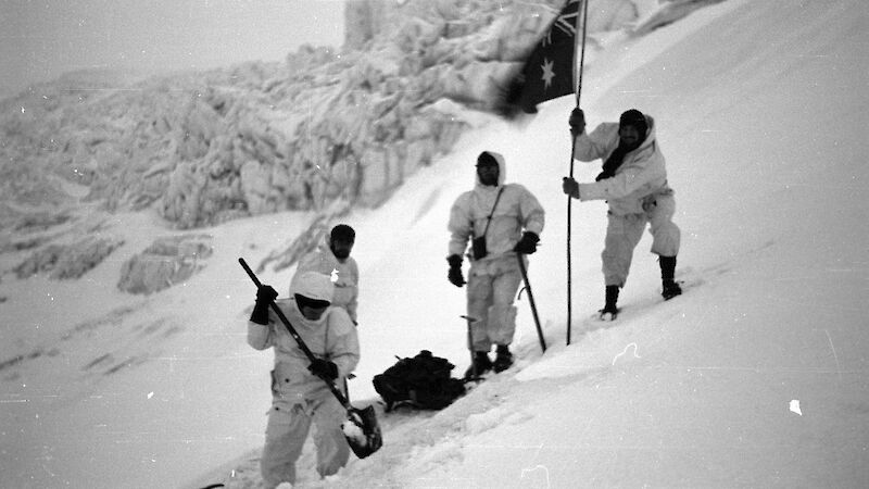 Black and white image of expeditioners planting flag and digging in to ice set up camp during the second attempt to climb Big Ben