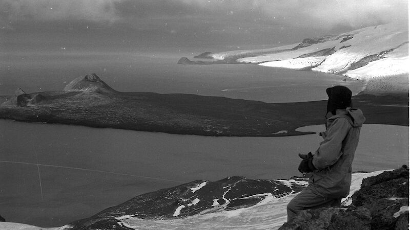 Black and white image of expeditioner and elevated view of peninsula and ice covered coast