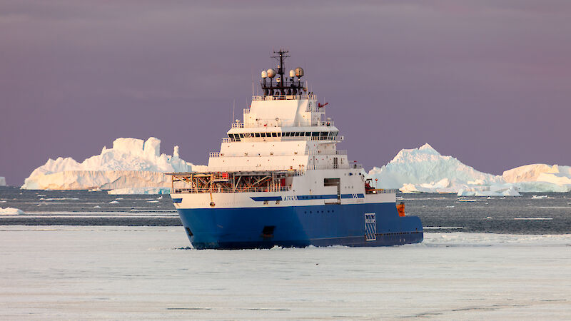 A blue and white ship breaks through sea ice.