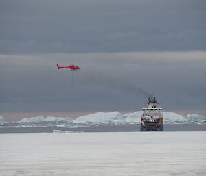 A blue and white ship and a red helicopter off an icy coast.