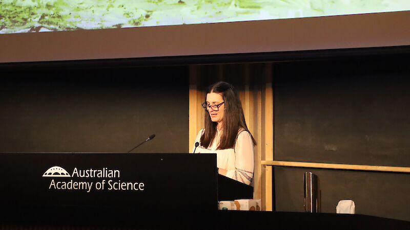 A woman stands at a lectern on stage at the Shine Dome in Canberra