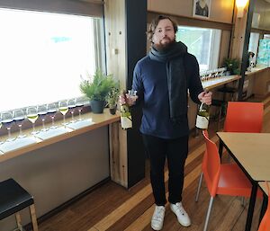 A man standing inside an Antarctic station with a couple of bottles of wine