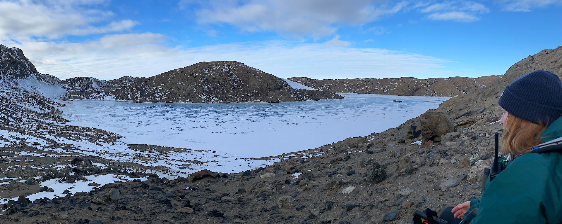 A person in a green jacket and blue beanie looking out onto a snowy lake